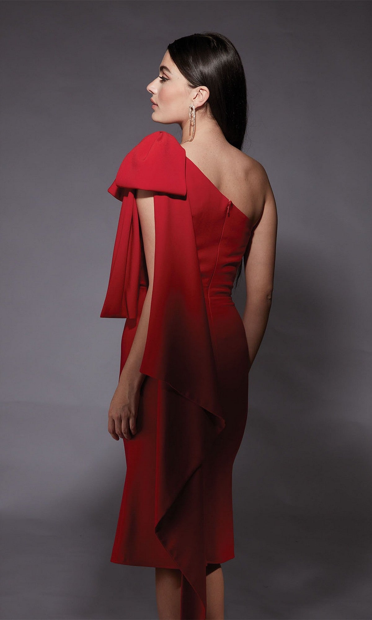 Woman models the Alyce 70053 Knee Length Semi-Formal Dress, a fitted, one-shoulder cocktail style with draped fabric accent, shown from the back against a plain gray background.